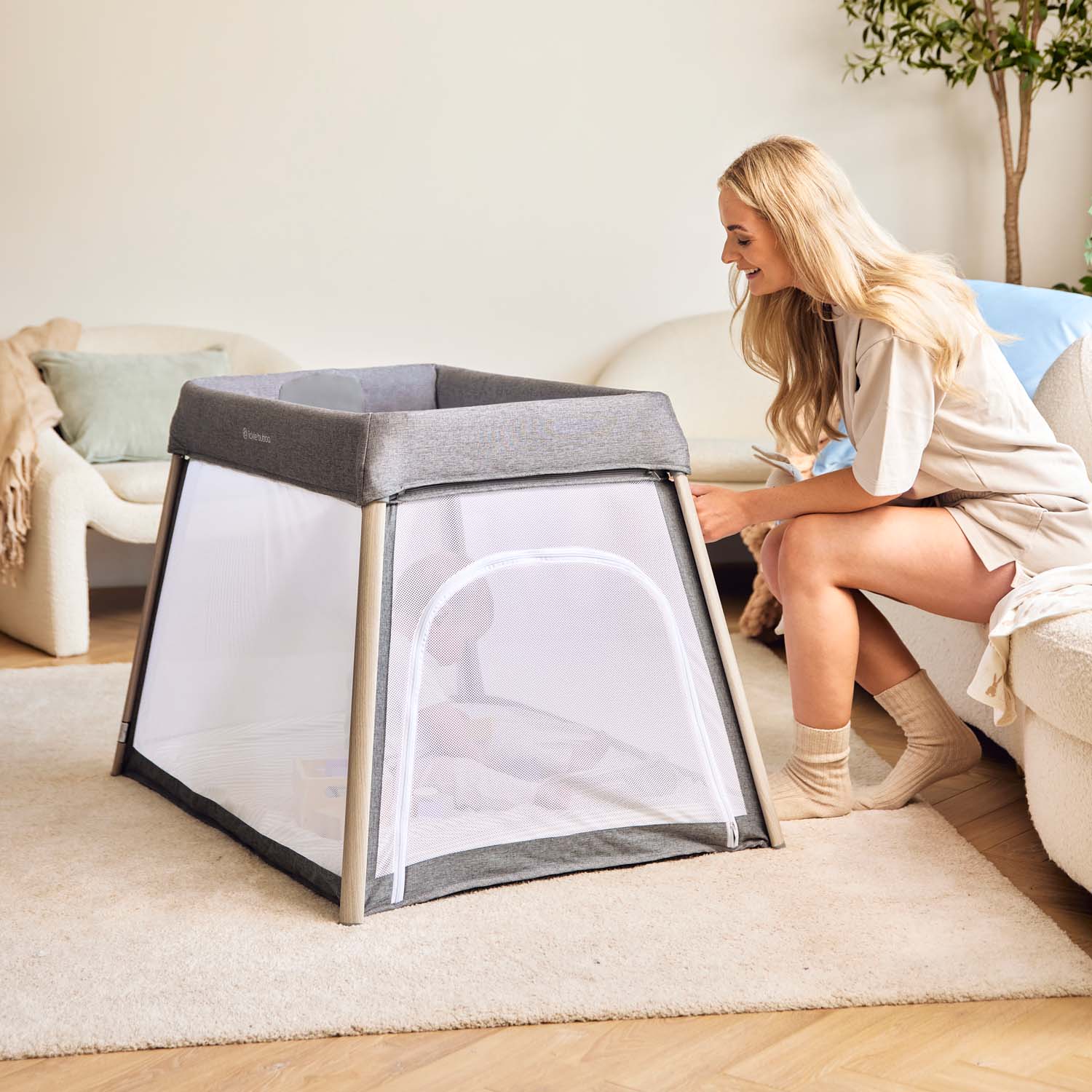 happy mom looking over her baby sitting inside the Ickle Bubba Scout 2-in-1 Travel Cot and Playpen