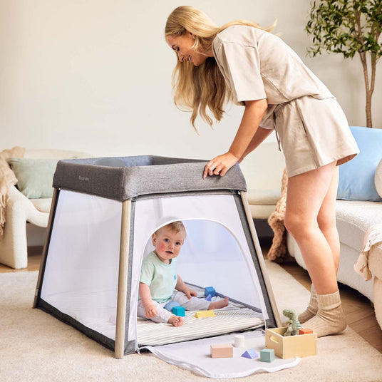 Happy mom checking her baby sitting inside the Ickle Bubba Scout 2-in-1 Travel Cot and Playpen