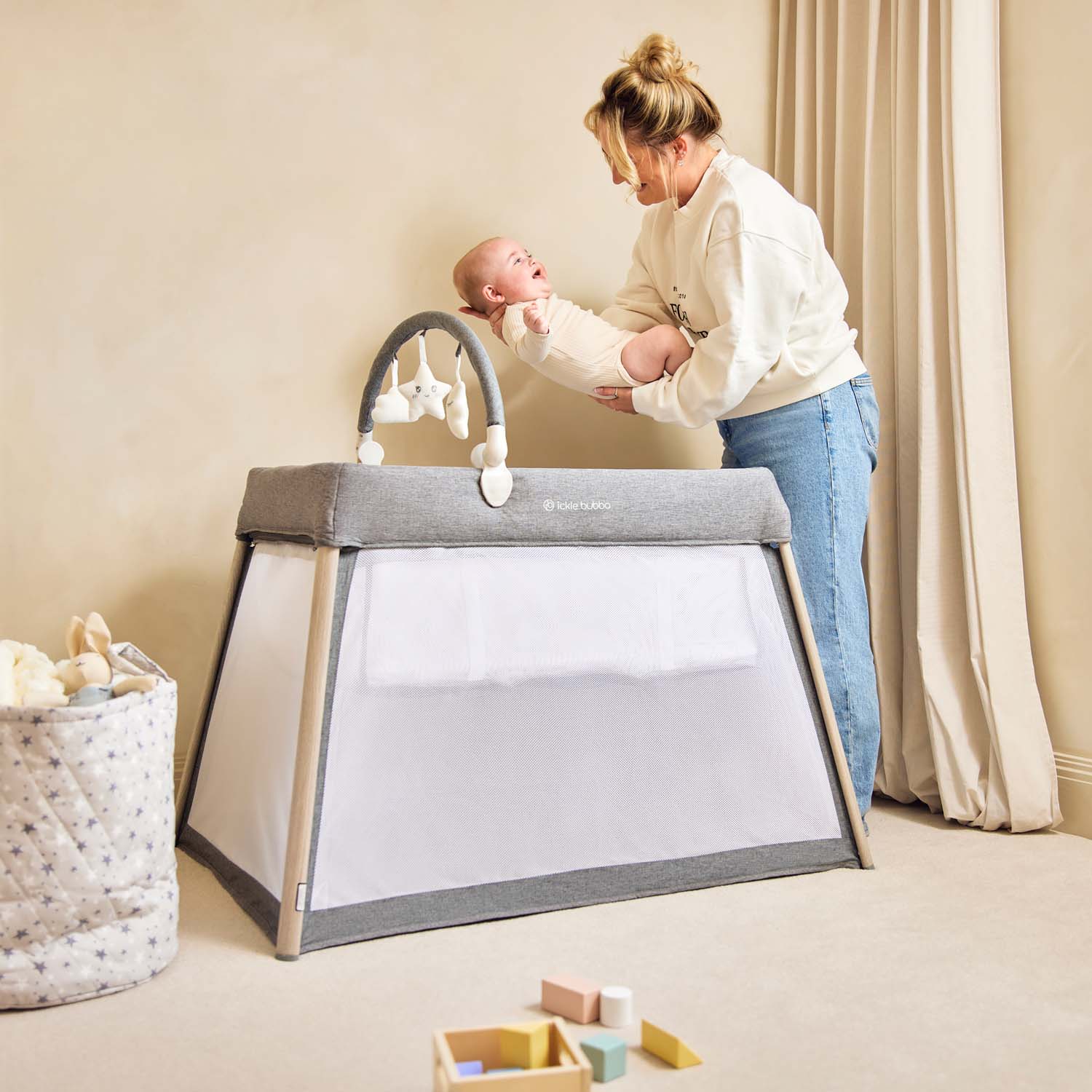 happy mom putting her baby inside the Ickle Bubba Scout 2-in-1 Travel Crib, Cot and Playpen