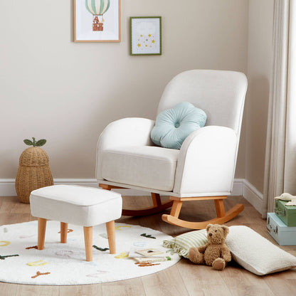 An angled shot of Babymore Freya Nursing Chair with Stool Set in Cream colour in a corner of a nursery room with a teddy bear and throw pillows on the floor.