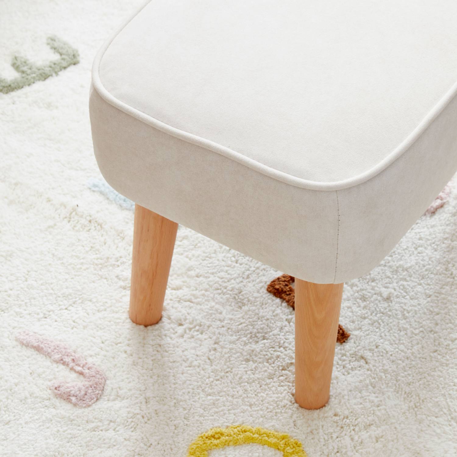 A close-up shot of the included Babymore Freya Footstool in Cream color showing the natural solid beech wood legs. 