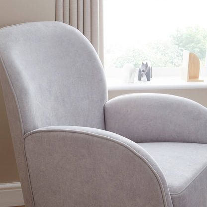 A close-up shot of Babymore Freya Nursing Rocking Chair in Grey colour showing the curved ergonomic design with supportive armrests in a nursery room and beside a window on its right side.