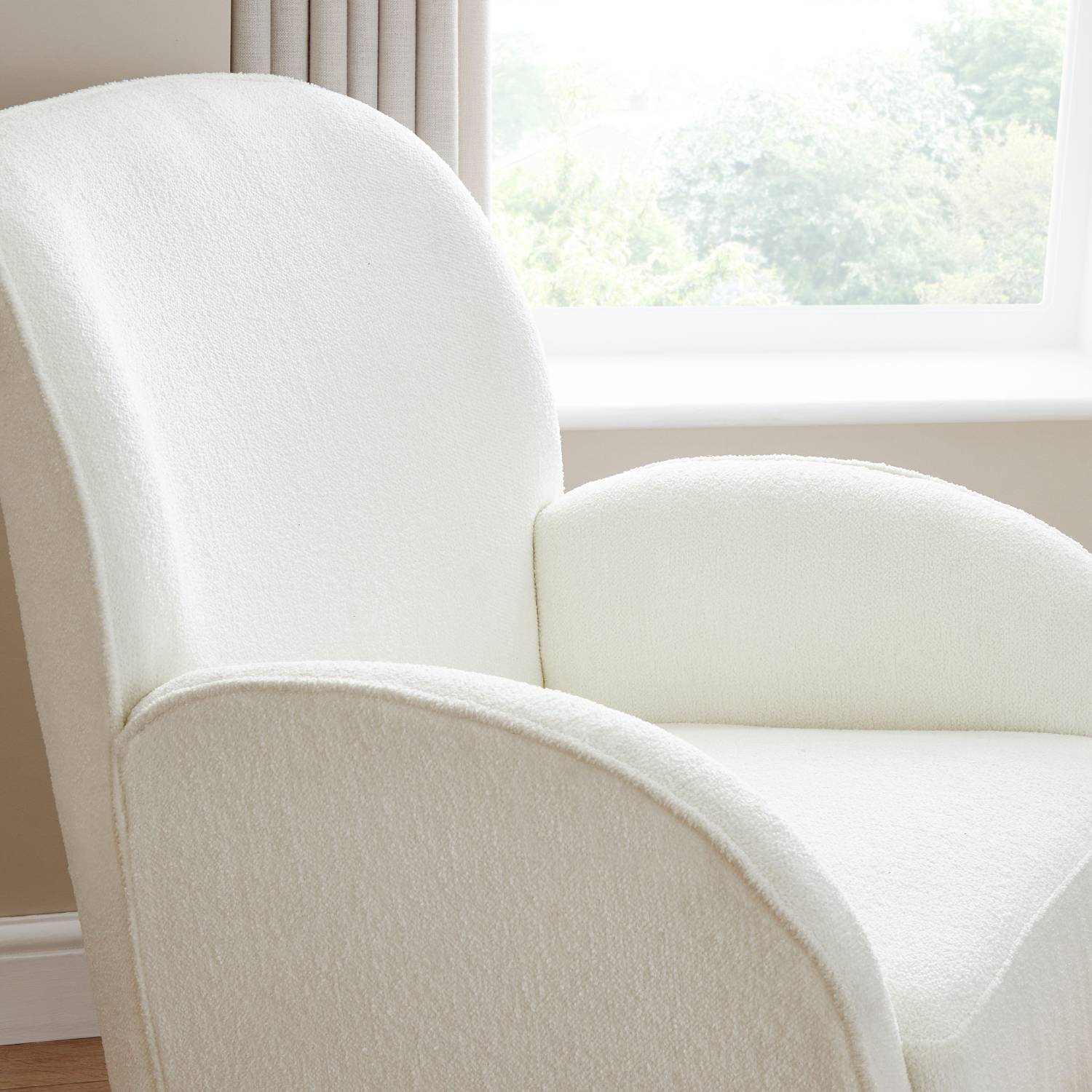 A close-up shot of Babymore Freya Nursing Rocking Chair in Off White Boucle colour showing the curved ergonomic design with supportive armrests beside a window on its right side.