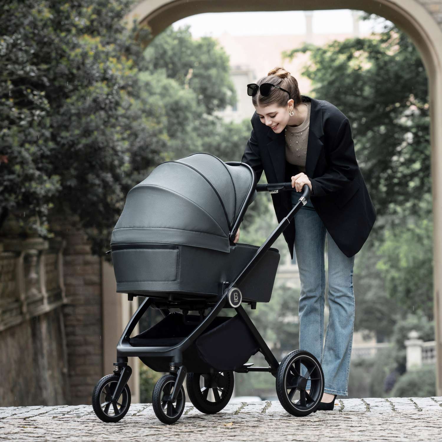 a woman pushing a Babymore Kai with carrycot in Forest Grey variant