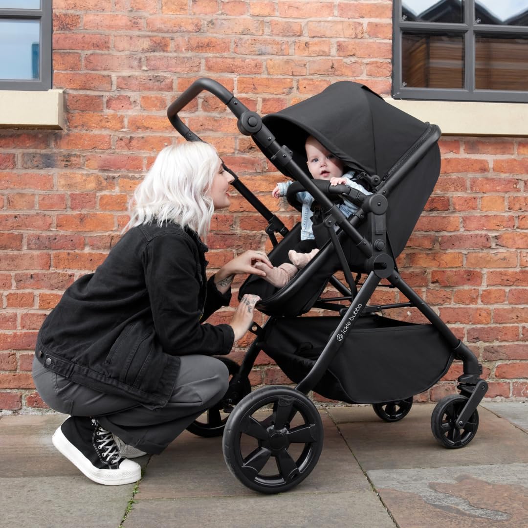A mother holding her baby beside an Ickle Bubba Comet 3-in-1 Travel System pushchair in Black colour