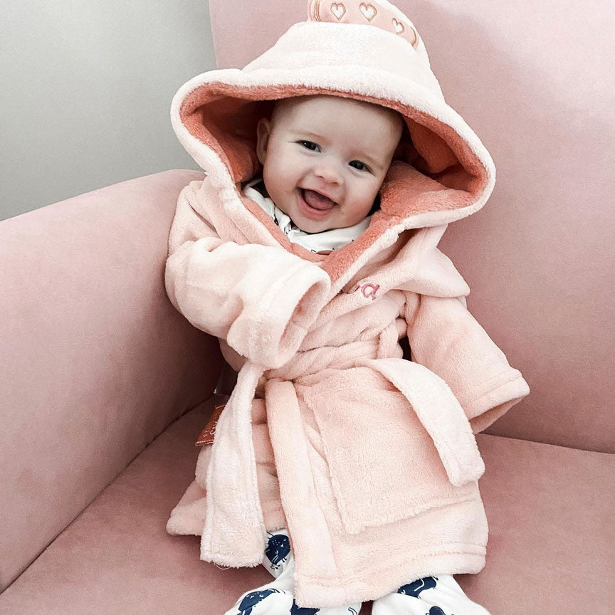 A happy baby sitting on Ickle Bubba Dursley Rocking Chair in Blush Pink colour