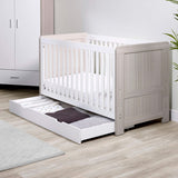 Angled lifestyle shot of Ickle Bubba Pembrey Cot Bed with opened Under Drawer storage full of clothes in Ash Grey and White colour