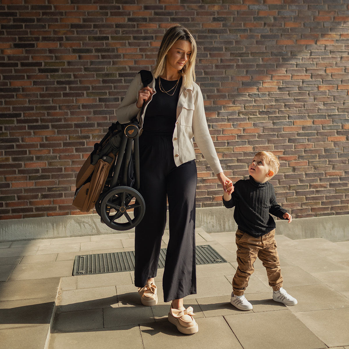 A mother holding her baby boy while carrying a Caramel Venicci Claro 3-in-1 Travel System