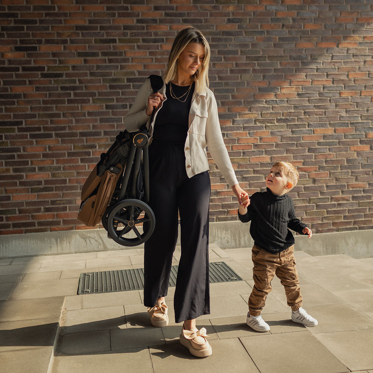 A mother holding her baby boy while carrying a Caramel Venicci Claro 2-in-1 Pram