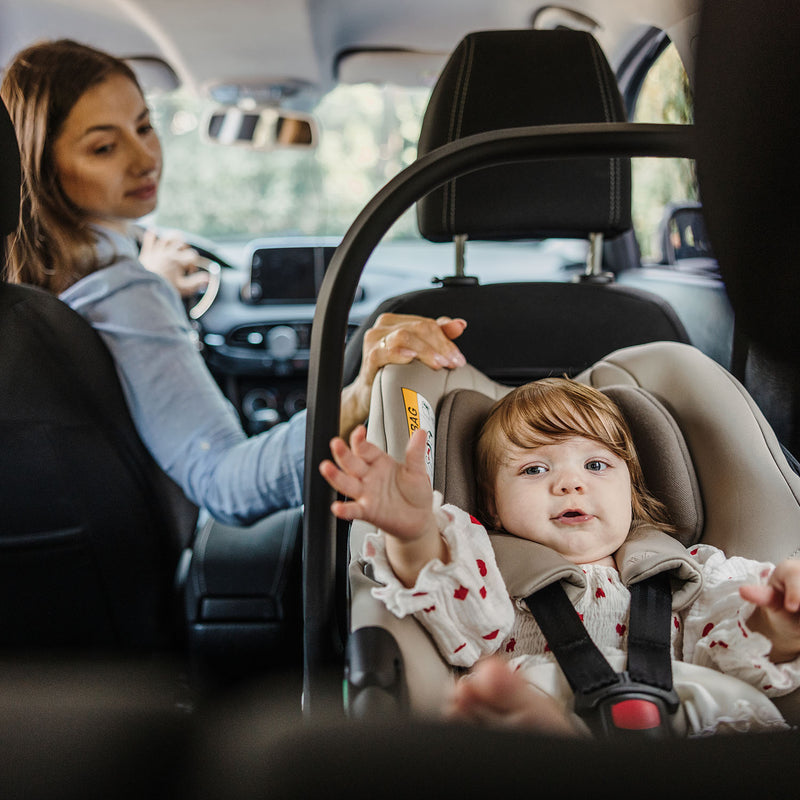 Mom sitting in drivers seat looking back at her baby safely buckled in Venicci Tiago car seat