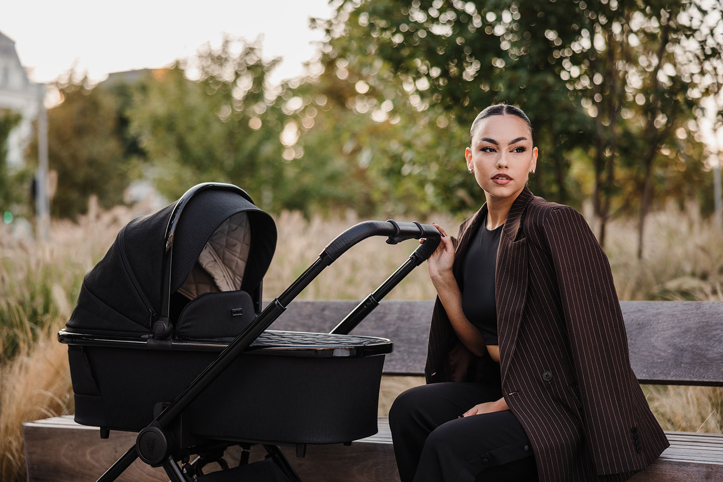 a woman sitting on a bench beside a Venicci Tinum Edge SE Pram in Raven black colour