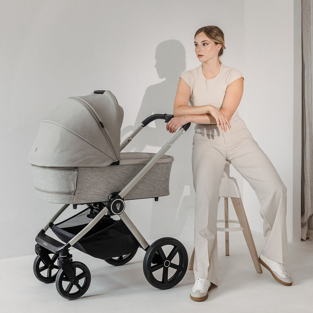 A woman sitting on a bar chair with a Venicci Upline 2-in-1 Pram in Moonstone colour on her side