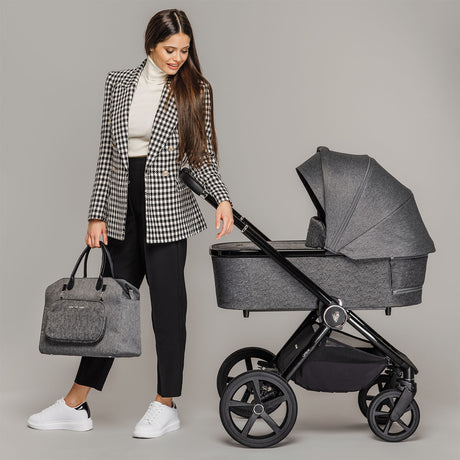 A woman holding the Upline Changing Bag beside a Venicci Upline 2-in-1 Pram in Slate Grey colour